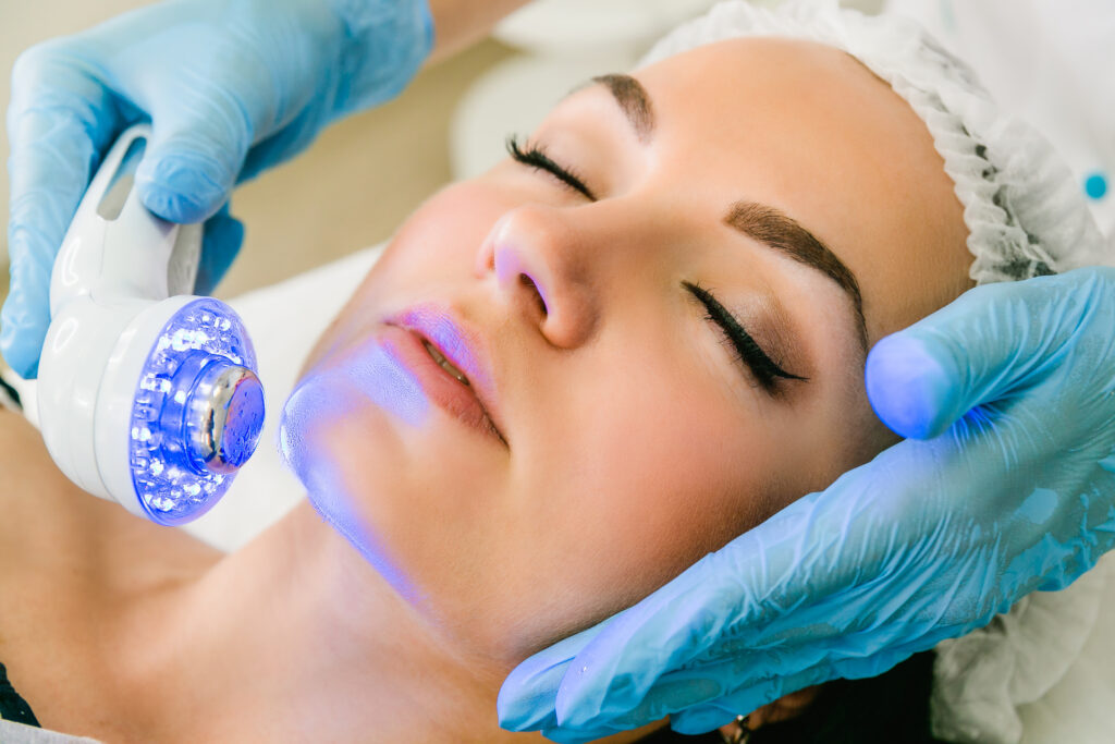 Close-up of a skincare professional using a blue light therapy device on a client’s face, advanced skincare treatment by Elite 360.